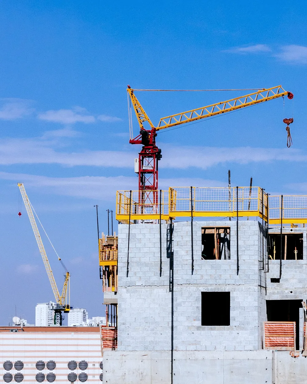 Edifício em construção com grua de torre ao fundo de céu azul